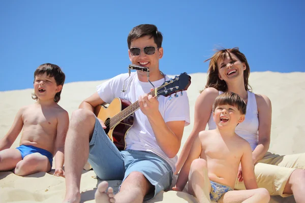 Парень в солнечных очках играет на гитаре и губной гармошке с детьми — стоковое фото
