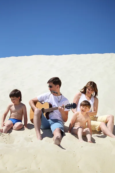 Парень в солнечных очках играет на гитаре и губной гармошке с детьми — стоковое фото