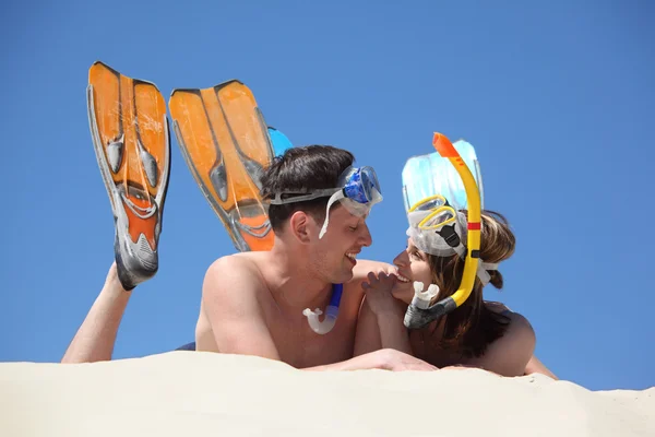 Coppia giovane in pinne e maschere subacquee giace sulla sabbia — Foto Stock