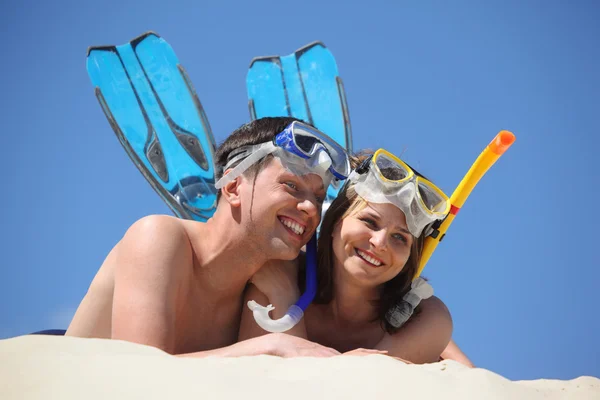 Young pair in fins and underwater masks lies on sand — Stock Photo, Image