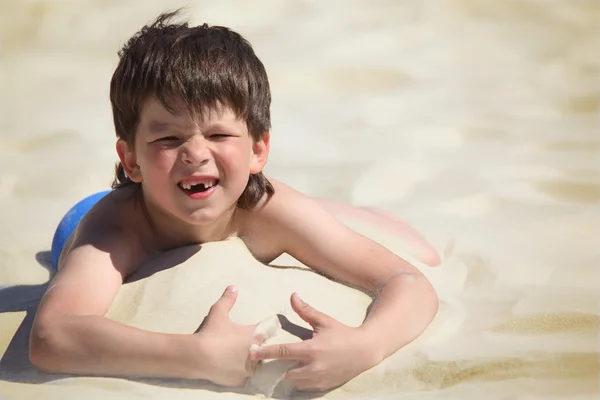 Pojke utan foreteeth ligger på sand — Stockfoto