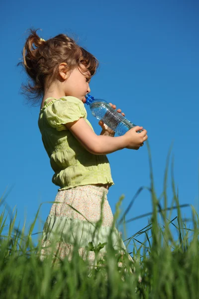 草の中に立っている女の子はプラスチック ボトルからの水を飲む — ストック写真