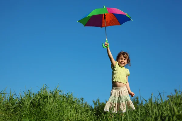 Flicka med mångfärgad paraply i lyft hand i gräs — ストック写真