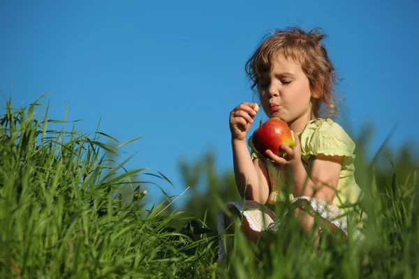 Lány piros Alma eszik fű, kék ég ellen — Stock Fotó