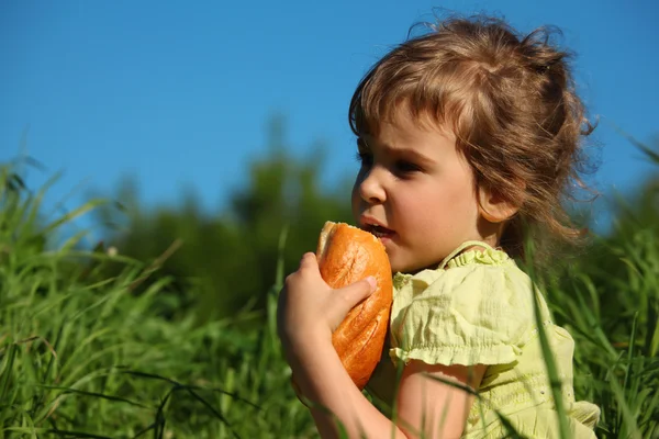 Girl eats bread in grass against blue sky — Stock Photo, Image