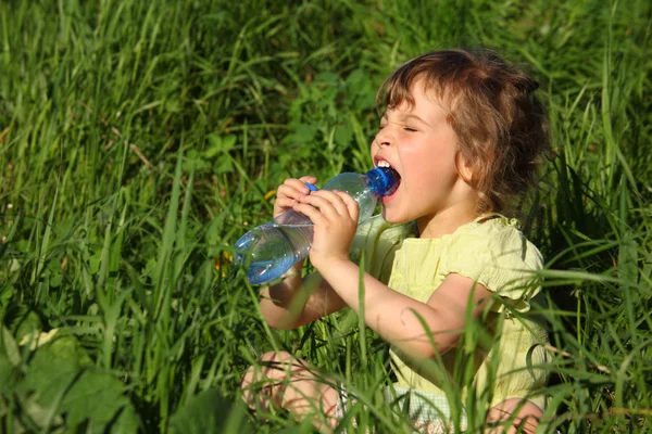 Girl sits in grass and drinks water from plastic bottle — Stock Photo, Image