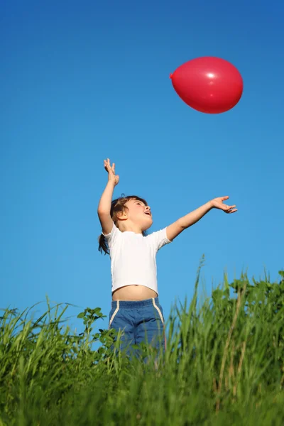 Klein meisje speelt met rode ballon in gras — Stockfoto