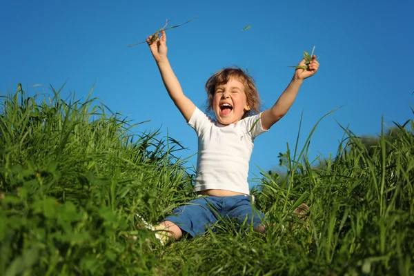 S úsměvem holčička sedí v trávě s zdvižené ruce — Stock fotografie