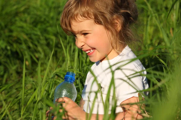 Niña sonriente en la hierba con botella de plástico —  Fotos de Stock