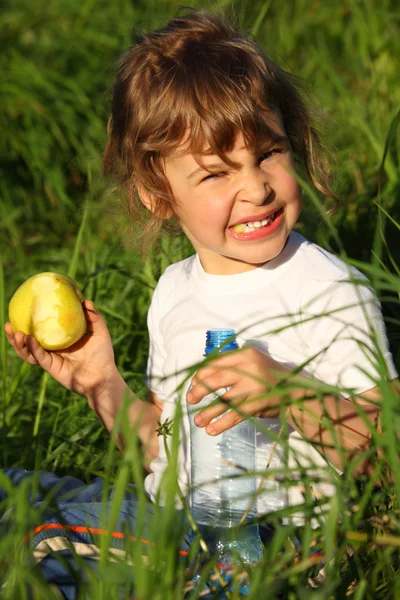 Flicka med plastflaska äter grönt äpple i gräs — Stockfoto