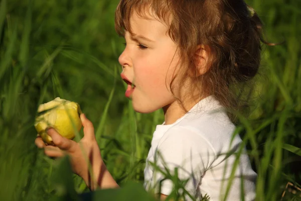Tjej äter grönt äpple i gräs — Stockfoto