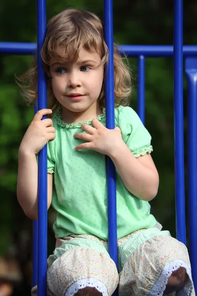 Маленька дівчинка сидить, тримаючись за захисні стрижні — стокове фото