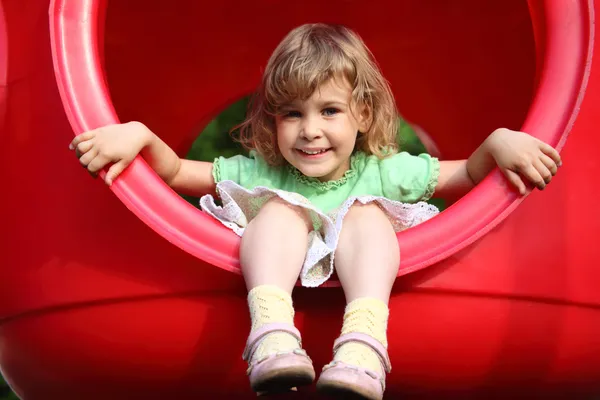 Маленька дівчинка сидить у червоній пластиковій дірі на дитячому майданчику — стокове фото