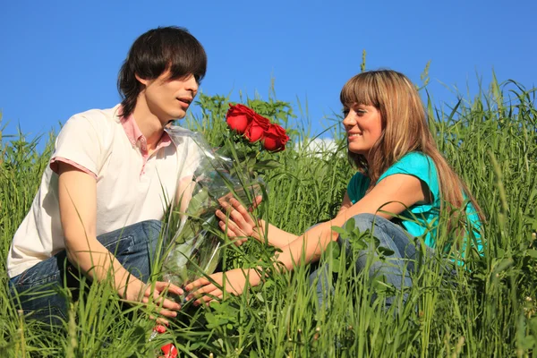 Guy gives to girl bouquet of roses among grass — Stock Photo, Image