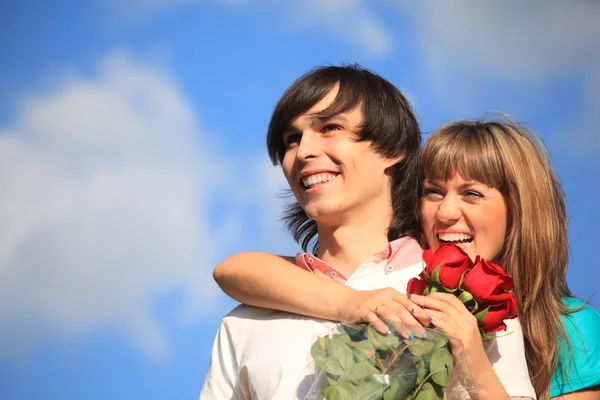 Dziewczyna z bukietem róż obejmuje za facet przed niebo — Zdjęcie stockowe