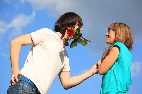 Парень с розой во рту и девушка на фоне неба — стоковое фото
