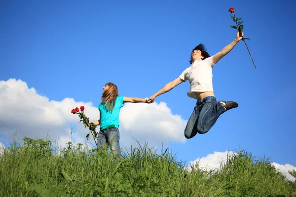 Guy with rose jumps holding girl with roses by hand — Stock Photo, Image