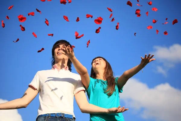 Mladá dvojice rozptýlí lístky růží proti obloze — Stock fotografie