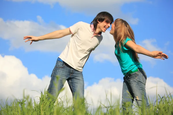 Laughing young pair looks against each other in grass against s — Stock Photo, Image
