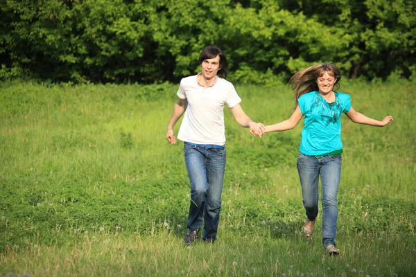 Unga par körs, hålla för händer, på gräset i parken — Stockfoto