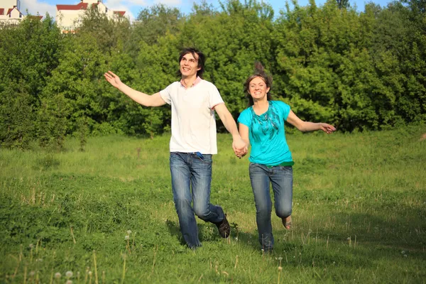 Leende unga par körs, hålla för händer, på gräset i parken — Stockfoto