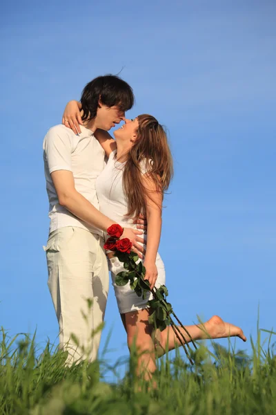 Girl with bouquet of roses kisses guy on grass against sky — Stock Photo, Image