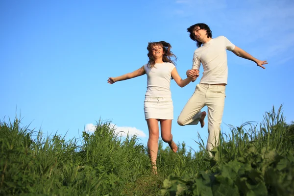 Молодая пара бегает держа руки на траве — стоковое фото