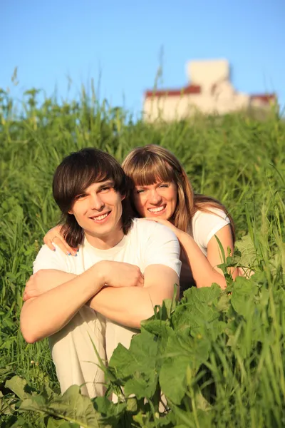 Girl embraces guy behind for shoulders among grass — Stock Photo, Image