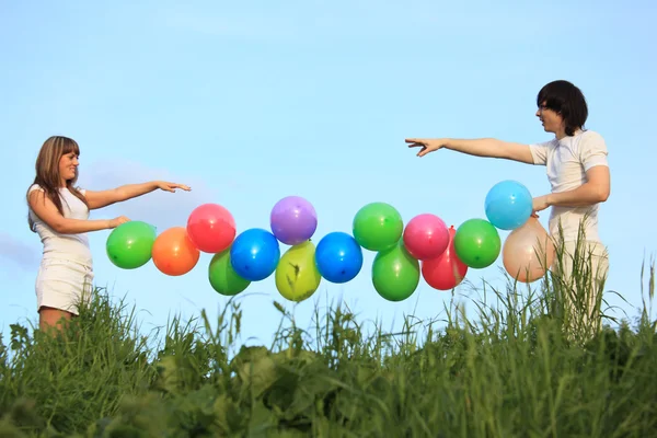 Girl and guy hold garland of multicoloured balloons in grass ag