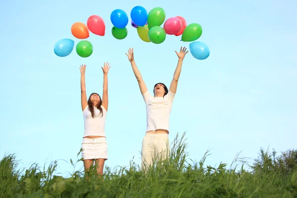Menina e cara começar balões multicoloridos no céu — Fotografia de Stock