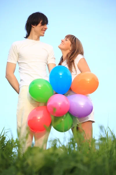 Menina e cara ficar na grama com balões multicoloridos — Fotografia de Stock