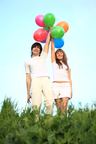 Girl and guy stand in grass with multicoloured balloons over hea — Stock Photo, Image