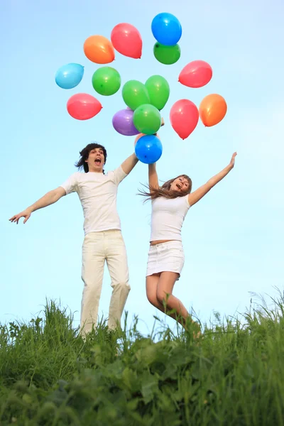 Menina e cara começar balões multi-coloridos no céu — Fotografia de Stock