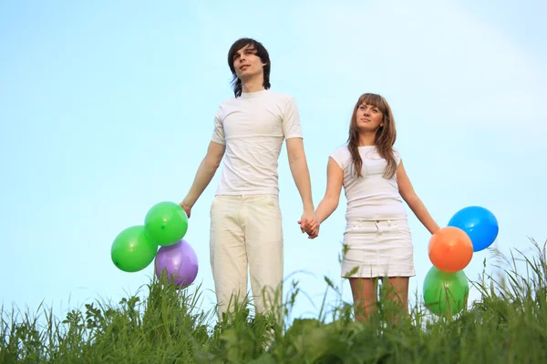 Girl and guy stand in grass with multicoloured balloons in hands — Stock Photo, Image