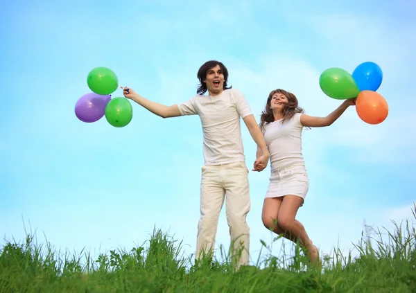 Girl and guy stand in grass with multicoloured balloons in hands — Stock Photo, Image