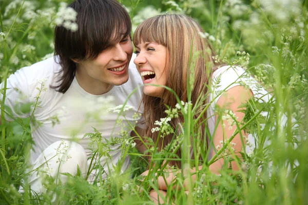Směje se mladý pár sedí v trávě — Stock fotografie