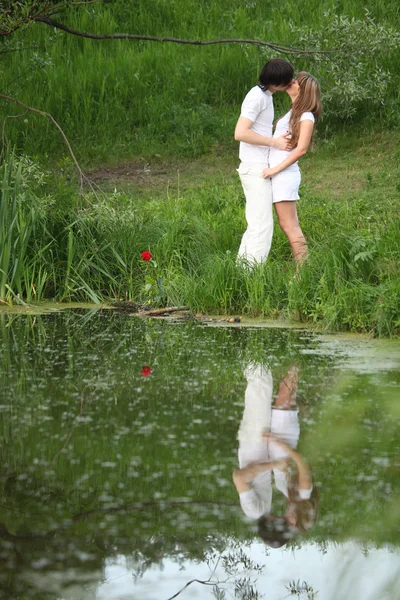 Young pair kisses on bank of pond — Stock Photo, Image