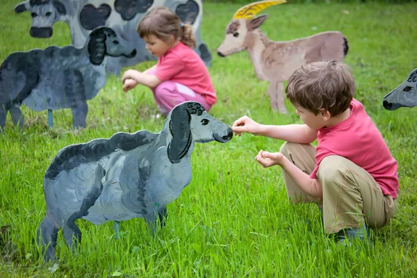A menina e o menino alimentam um animal de madeira — Fotografia de Stock