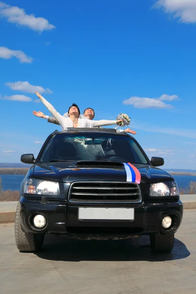 Noivo e noiva estão felizes de pé no carro — Fotografia de Stock