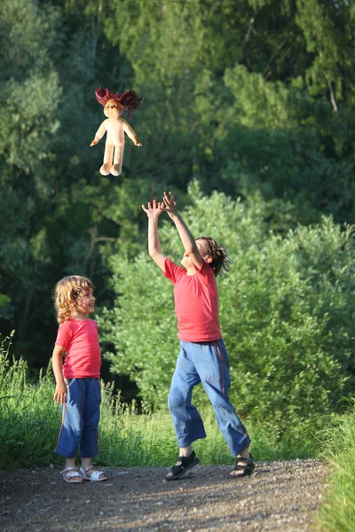 Niño y niña en el parque arrojar hacia arriba muñeca — Foto de Stock