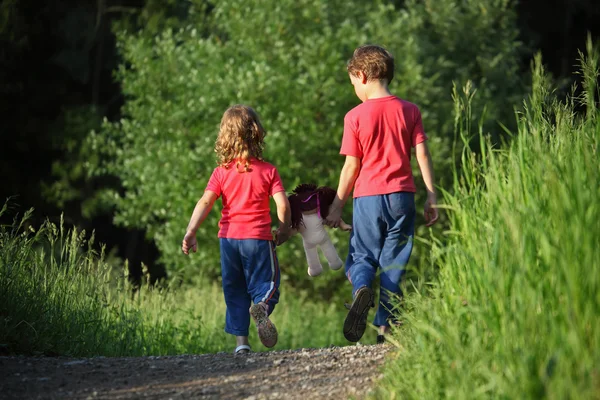 Chlapec a dívka jít na procházku s panenkou v parku, pohled zezadu — Stock fotografie