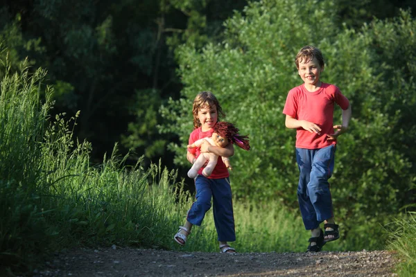Menino e menina correr com boneca no parque — Fotografia de Stock
