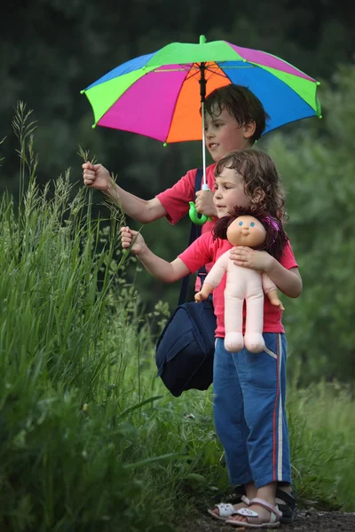Menino e menina sob guarda-chuva no parque rasgar grama — Fotografia de Stock