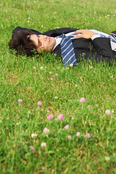 İş adamı çimenlerin üzerinde gözleri kapalı yatıyor. — Stok fotoğraf