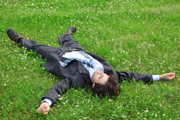 Podnikatel leží na zádech na trávě, mají natažené nohy a han — Stock fotografie