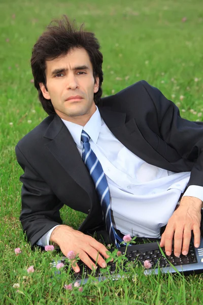 Podnikatel leží na trávě s notebookem — Stock fotografie