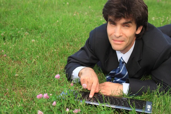 Homem de negócios sorrindo encontra-se na grama com laptop — Fotografia de Stock