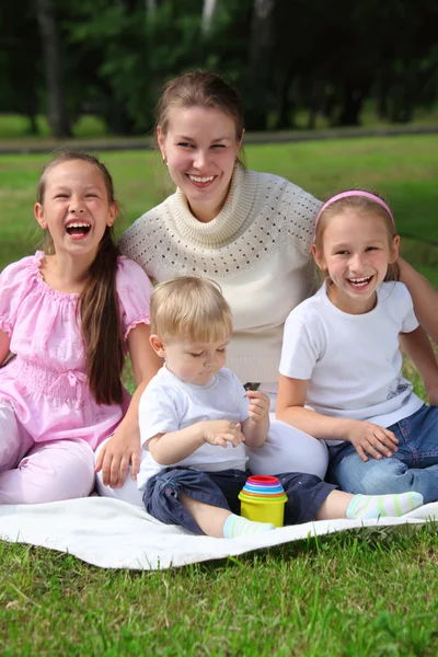 母親と子供たちを笑いながら草の上に敷設に座っています。 — ストック写真