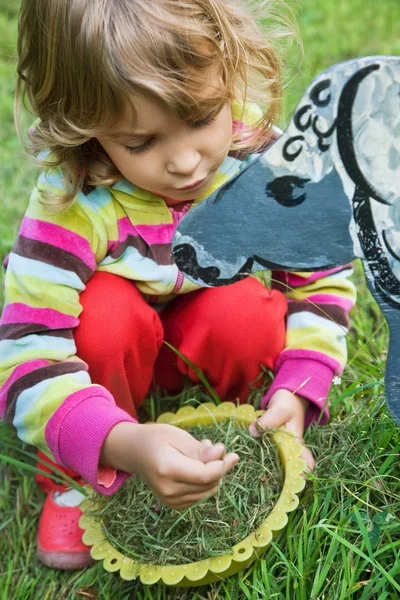 Hübsches kleines Mädchen füttert Holzpferd im Garten — Stockfoto