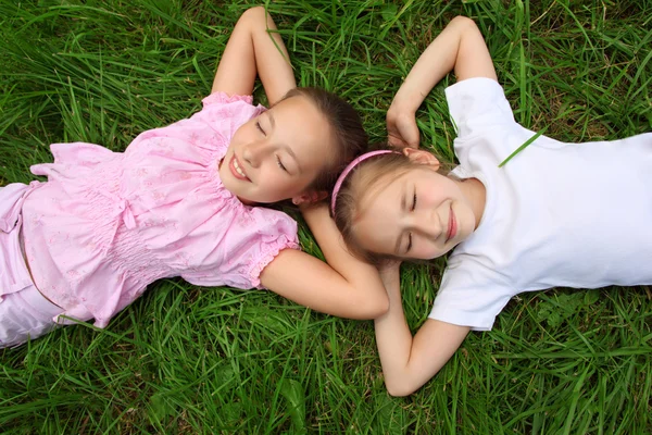 Dos chicas yacen en la hierba con los ojos cerrados, cabeza a cabeza —  Fotos de Stock